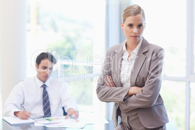 Serious businesswoman posing while her colleague is working