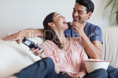 Playful couple watching TV while eating popcorn