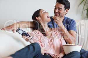 Playful couple watching TV while eating popcorn