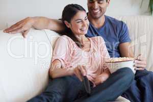 Delighted couple watching TV while eating popcorn