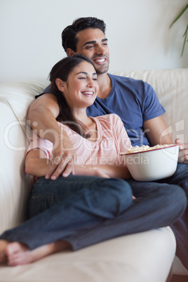 Portrait of a happy couple watching television while eating popc