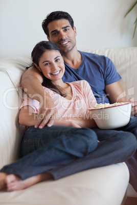 Portrait of a smiling couple watching television while eating po