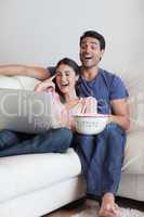 Portrait of a laughing couple watching a movie while eating popc