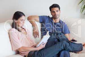 Woman reading a book while her boyfriend is watching television