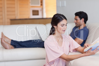 Woman reading a book while her fiance is using a laptop