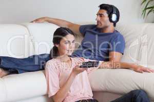 Woman watching TV while her fiance is listening to music