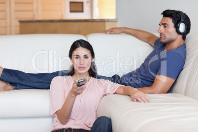 Woman watching television while her boyfriend is listening to mu