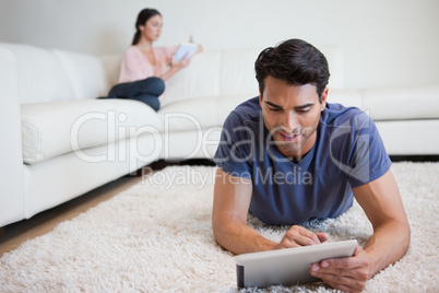 Man using a tablet computer while his girlfriend is reading a bo
