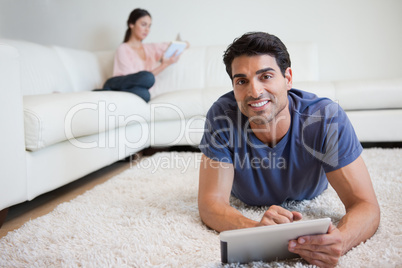Man using a tablet computer while his fiance is reading a book