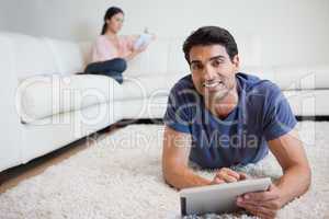 Man using a tablet computer while his fiance is reading a book