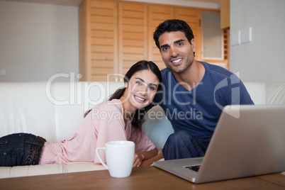 Smiling couple using a laptop while having a tea