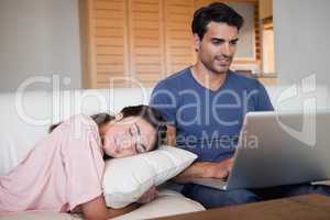 Man using a laptop while his fiance is sleeping