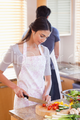 Portrait of a woman chopping pepper while her fiance is washing