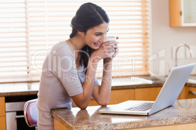 Lovely woman using a laptop while drinking a cup of a coffee