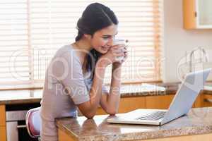 Lovely woman using a laptop while drinking a cup of a coffee