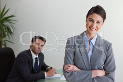 Happy businesswoman posing while her colleague is working