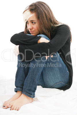 Sad girl teenager sits twining arms about legs. Isolated on a wh