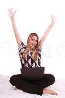 Woman sitting on the bed with a laptop computer and arms up - is