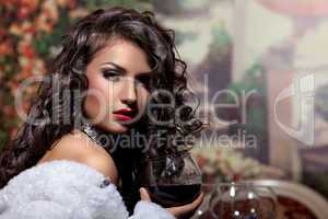 Sexy girl sit with wine in fur coat at evening