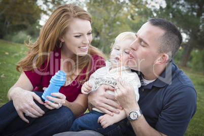 Young Parents Blowing Bubbles with their Child Boy in Park Young Parents Blowing Bubbles with their Child Boy in Park