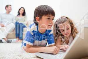 Kids using laptop on the carpet with parents behind them