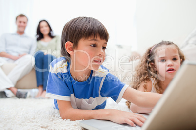 Kids playing computer games on the carpet with parents behind th