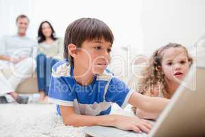 Kids playing computer games on the carpet with parents behind th