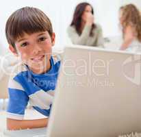 Boy using laptop on the carpet with his family behind him
