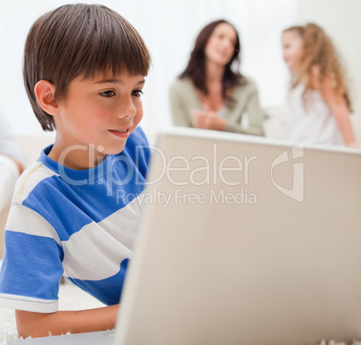 Boy playing computer games with his family behind him