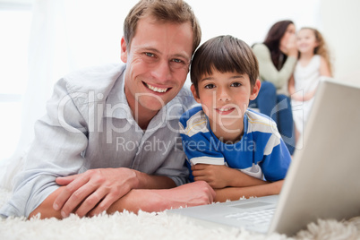 Smiling son and dad using laptop on the carpet