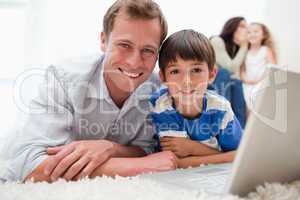 Smiling son and dad using laptop on the carpet