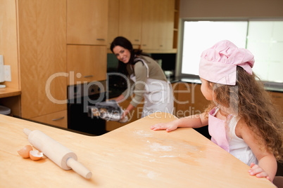 Girl watching her mother putting cookies into the oven