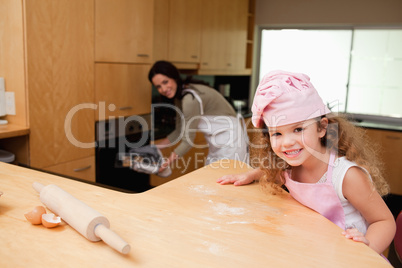 Girl sitting in the kitchen while her mother puts cookies into t