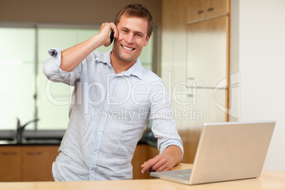 Man with cellphone and laptop in the kitchen