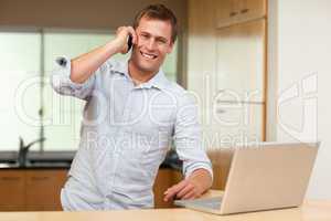 Man with cellphone and laptop in the kitchen