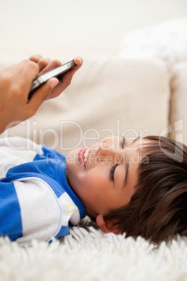 Boy playing with his cellphone while lying on the carpet
