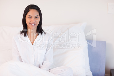 Smiling woman in pajamas sitting on her bed