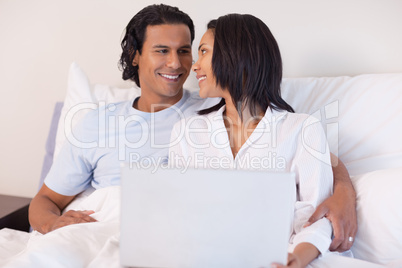 Young couple sitting on the bed with their laptop