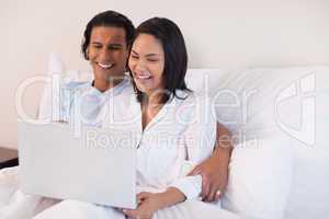 Couple using their laptop while sitting on the bed