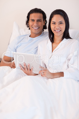 Couple using tablet pc in their bed