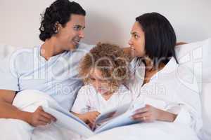 Family sitting on the bed reading a book