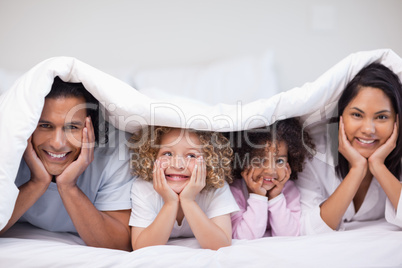 Smiling family hiding under the blanket