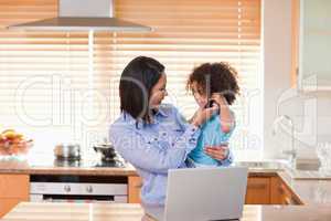 Mother and daughter using laptop and cellphone in the kitchen to