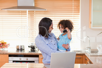 Mother and daughter using notebook and cellphone in the kitchen