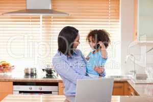 Mother and daughter using notebook and cellphone in the kitchen