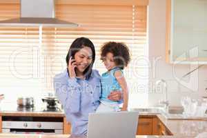 Mother and daughter using cellphone and laptop in the kitchen to