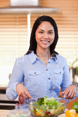 Smiling woman in the kitchen stirring salad