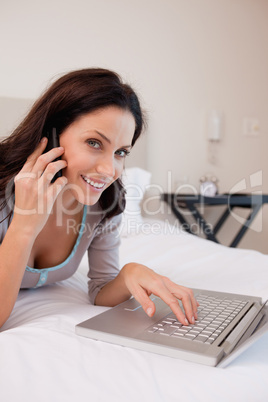 Side view of smiling woman with laptop and phone on the bed