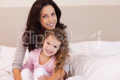 Mother hugging her daughter on the bed