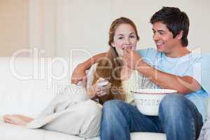 Happy couple watching television while eating popcorn